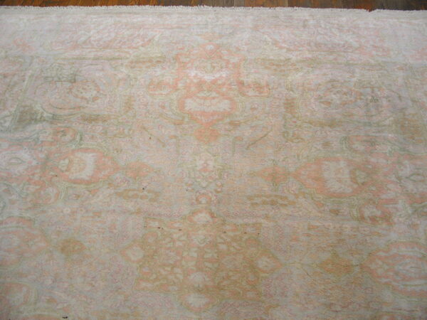 Low-pile distressed rug featuring traditional patterns in faded coral, ivory, and muted green on wood floor.