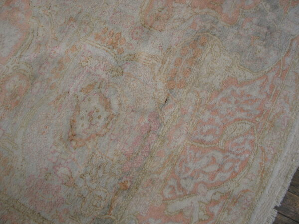 High-pile rug featuring a distressed traditional pattern in soft pink and gray on dark wood floor.