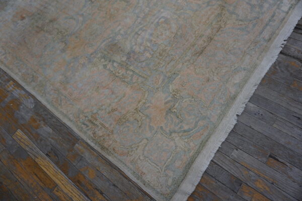 Low-pile traditional rug featuring faded blue and blush tones and white fringe on distressed wood.