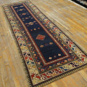 Traditional navy runner with geometric patterns in red and gold resting on golden plank flooring.