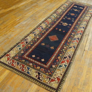 Low-pile runner rug with a navy blue field and multi-colored geometric borders sits on distressed hardwood.