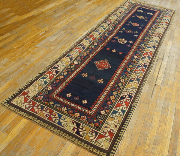 Low-pile runner rug with a navy blue field and multi-colored geometric borders sits on distressed hardwood.