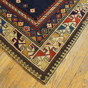Geometric rug corner featuring navy, red, blue, and tan patterns rests on light hardwood floors.