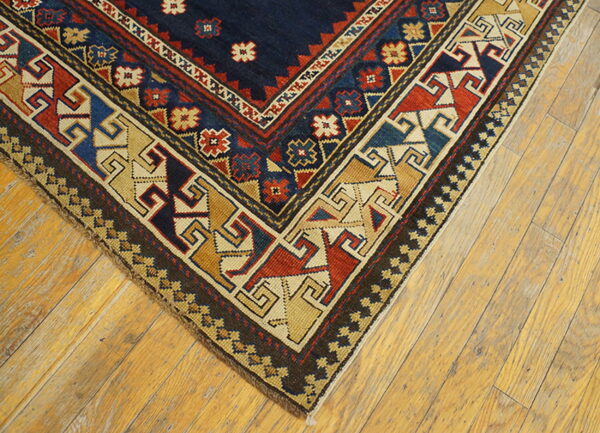 Geometric rug corner featuring navy, red, blue, and tan patterns rests on light hardwood floors.