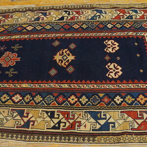 Geometric low-pile rug with a dark blue field and multi-colored borders laid across light wood flooring.