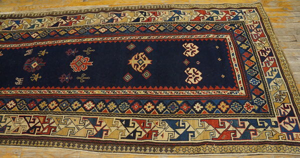 Geometric low-pile rug with a dark blue field and multi-colored borders laid across light wood flooring.