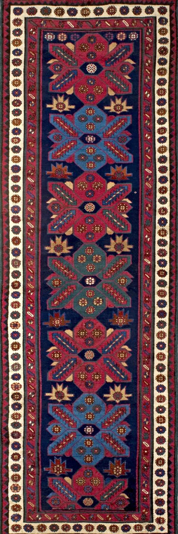 Narrow runner rug with geometric medallions in deep red, blue, and teal on a navy field.