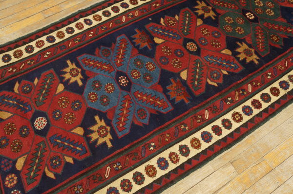 Navy, red, and blue geometric runner rug with complex borders rests diagonally on light wooden planks.