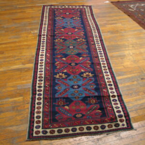 Long runner rug featuring red, blue, and cream geometric patterns sits on wood plank flooring.