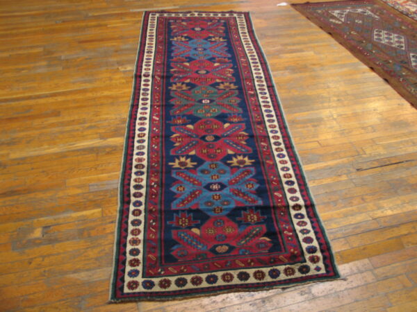 Long runner rug featuring red, blue, and cream geometric patterns sits on wood plank flooring.