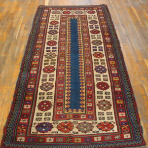 A long runner rug featuring a blue central stripe and cream panels with dense, colorful geometric motifs on wood flooring.