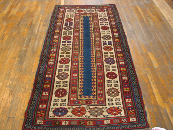 A long runner rug featuring a blue central stripe and cream panels with dense, colorful geometric motifs on wood flooring.