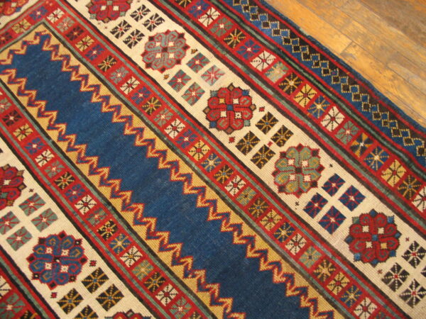 Blue, red, and cream geometric rug showing striped bands, medallions, and zigzag patterns on a wood floor.