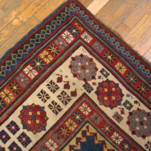 Geometric red, blue, and cream rug corner displaying multiple borders resting on light wooden plank floors.