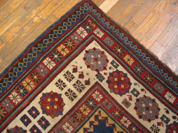 Geometric red, blue, and cream rug corner displaying multiple borders resting on light wooden plank floors.