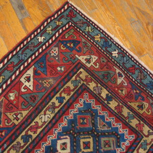Red, blue, and teal geometric rug corner displayed against honey-colored hardwood flooring.