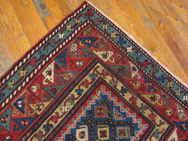 Red, blue, and teal geometric rug corner displayed against honey-colored hardwood flooring.