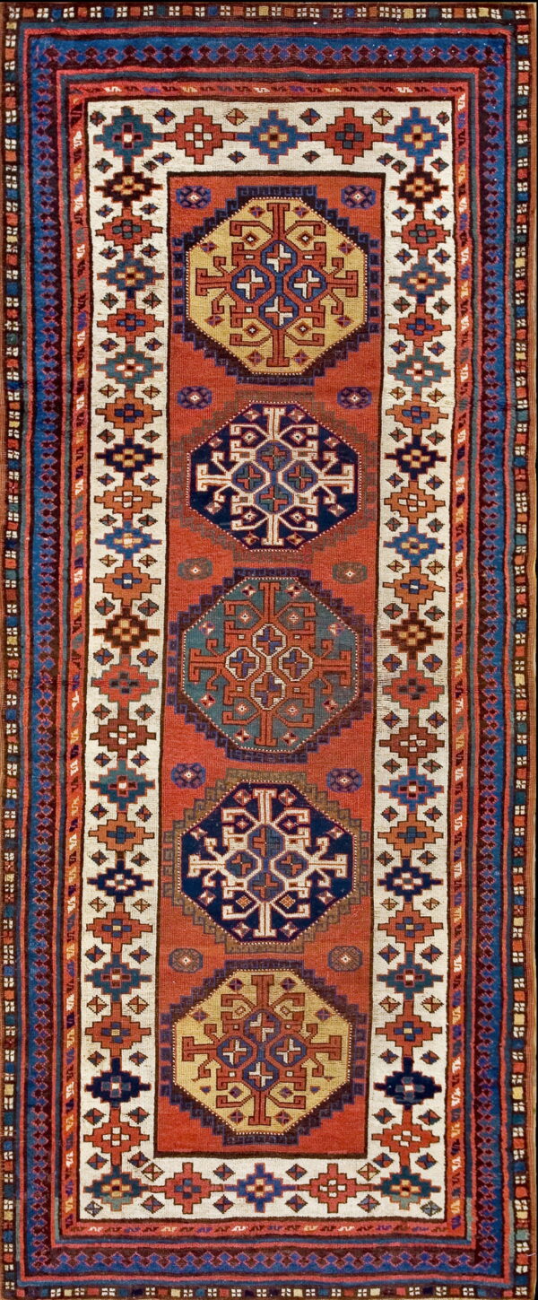 Vertical geometric runner rug in rust, navy, gold, and cream with repeating central tribal medallions.