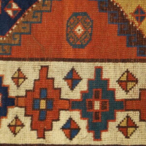 Detail of a low-pile rug showing geometric patterns in rust, cream, navy, and teal colors.