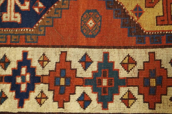 Detail of a low-pile rug showing geometric patterns in rust, cream, navy, and teal colors.