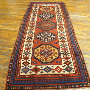 Geometric runner rug featuring rust red, navy, and cream medallions on distressed hardwood flooring.