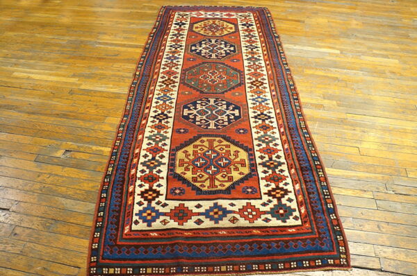 Geometric runner rug featuring rust red, navy, and cream medallions on distressed hardwood flooring.