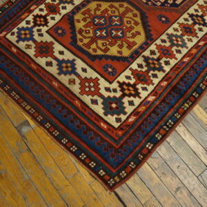 Geometric rug with rust, blue, and gold tribal patterns rests on distressed wooden floorboards.