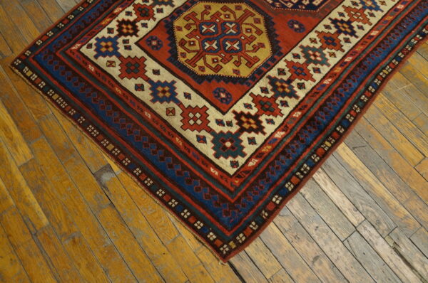 Geometric rug with rust, blue, and gold tribal patterns rests on distressed wooden floorboards.