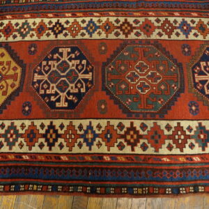 Geometric rust-red rug features large octagonal medallions in navy, gold, and green on wood flooring.