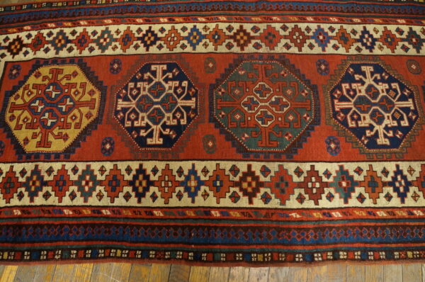 Geometric rust-red rug features large octagonal medallions in navy, gold, and green on wood flooring.