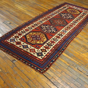 Red and blue tribal runner rug featuring three central medallions rests on worn wood planks.