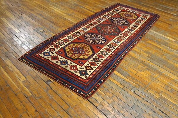 Red and blue tribal runner rug featuring three central medallions rests on worn wood planks.