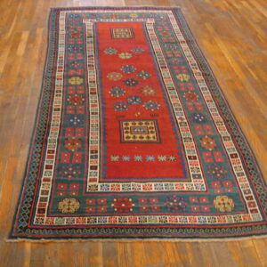 Red and teal runner rug featuring intricate geometric motifs is displayed on plank wood flooring.