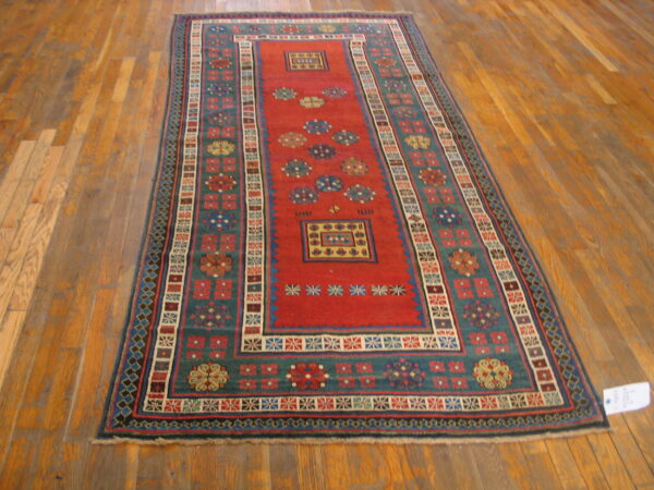 Red and teal runner rug featuring intricate geometric motifs is displayed on plank wood flooring.