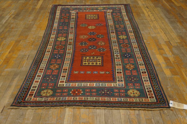 A long runner rug featuring a rust red field, teal border, and geometric motifs on distressed wood flooring.