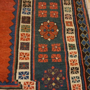 Geometric rug with rust, teal, and blue patterns, including stepped borders, resting on rustic wooden flooring.