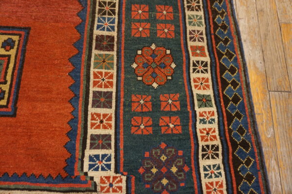Geometric rug with rust, teal, and blue patterns, including stepped borders, resting on rustic wooden flooring.