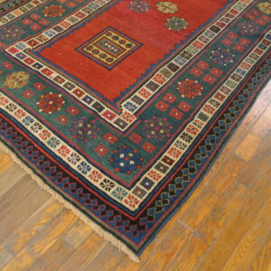 Geometric short-pile rug in red and teal with colorful medallions shown on wooden plank flooring.