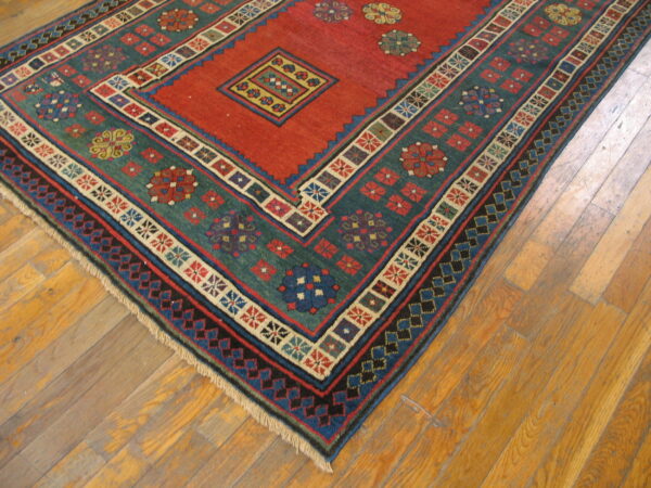 Geometric short-pile rug in red and teal with colorful medallions shown on wooden plank flooring.