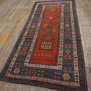 Geometric runner rug with a rusty red field and a broad teal border on weathered wood flooring.