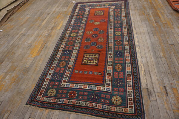 Geometric runner rug with a rusty red field and a broad teal border on weathered wood flooring.