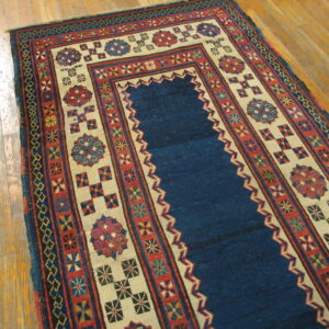 Geometric prayer rug in deep blue, red, and beige with tribal patterns on light wood flooring.
