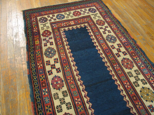 Geometric prayer rug in deep blue, red, and beige with tribal patterns on light wood flooring.