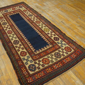 Geometric rug with a navy center and elaborate red and tan borders rests on distressed wood flooring.
