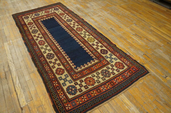 Geometric rug with a navy center and elaborate red and tan borders rests on distressed wood flooring.