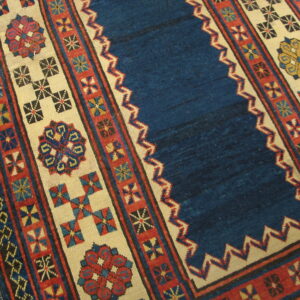 Low-pile rug with a blue center field and geometric borders in red, ivory, and contrasting colors on wood floor.