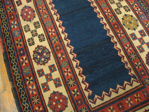 Low-pile rug with a blue center field and geometric borders in red, ivory, and contrasting colors on wood floor.