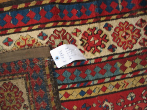 Red, blue, and cream low-pile rug displaying intricate geometric and stylized floral border patterns.