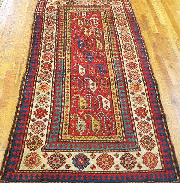 Low-pile geometric runner in red, cream, and blue with ornate borders on a polished wood floor.