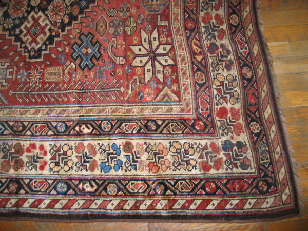 Red and cream rug with complex geometric patterns and a detailed border, resting on hardwood flooring.